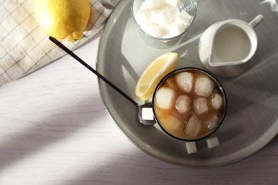 Photo of Refreshing iced coffee with milk in glass, sugar cubes and spoon on white wooden table, top view. Space for text