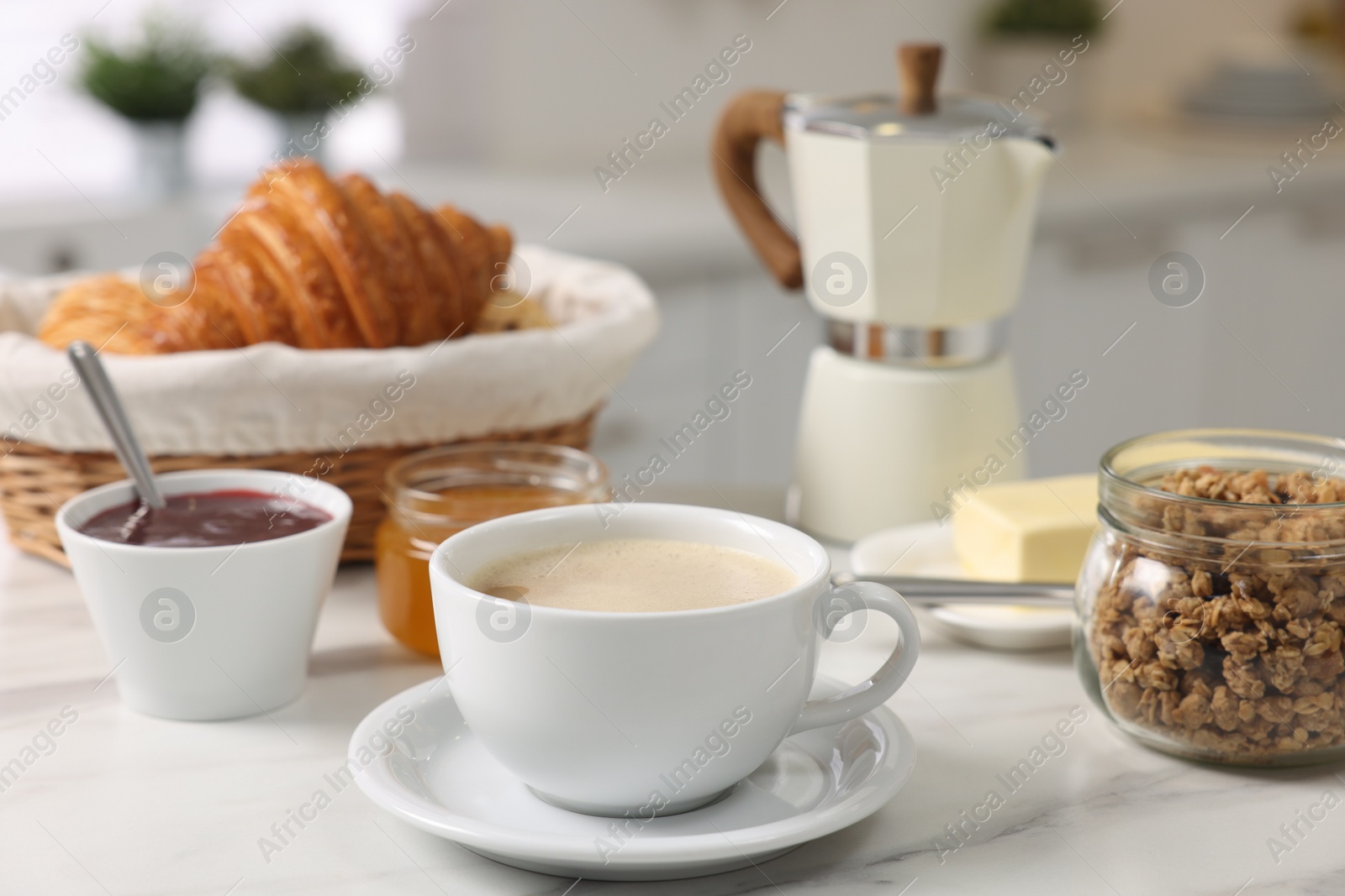 Photo of Breakfast served in kitchen. Fresh coffee, granola, croissants, jam and honey on white table