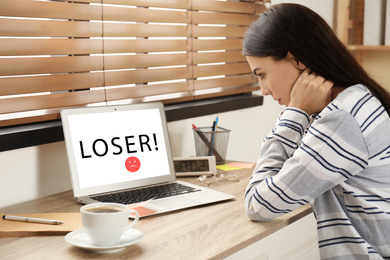 Young woman using laptop at wooden table. Cyber bullying