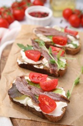 Delicious bruschettas with anchovies, tomatoes, microgreens and cream cheese on table, closeup