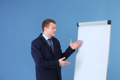 Photo of Business trainer giving presentation on flip chart board against color background