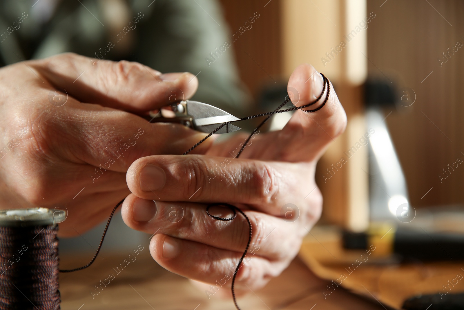 Photo of Man cutting thread while working with leather at table, closeup