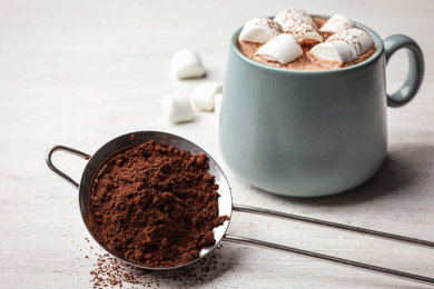 Strainer with cocoa powder and cup of hot drink on white wooden table