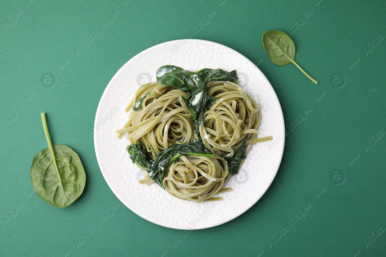 Photo of Tasty pasta with spinach and sauce on green table, flat lay