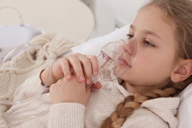 Photo of Little girl using nebulizer for inhalation indoors, closeup