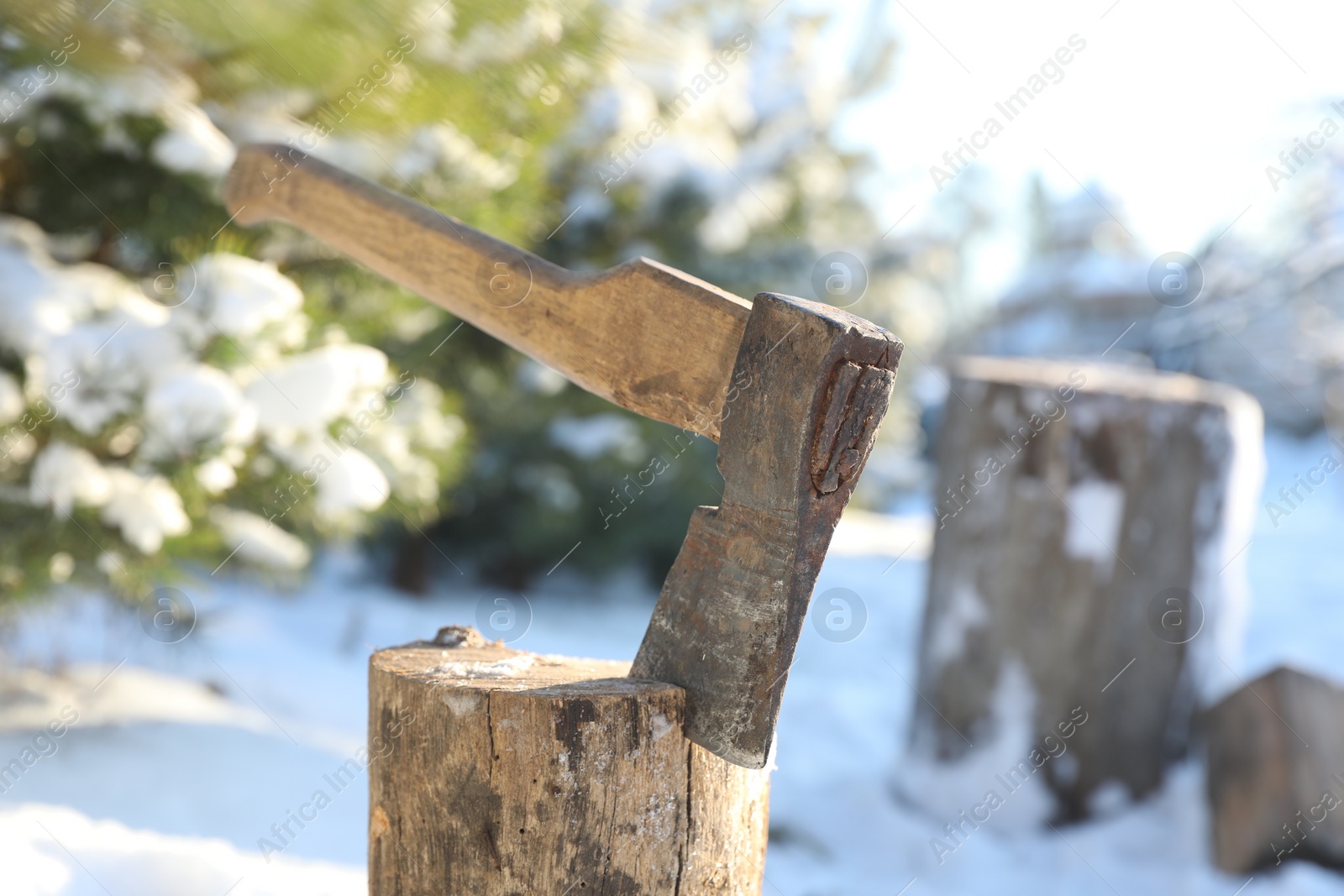 Photo of Metal axe in wooden log outdoors on sunny winter day, closeup