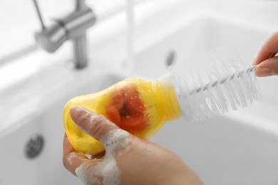 Woman washing baby bottle with brush in kitchen, closeup