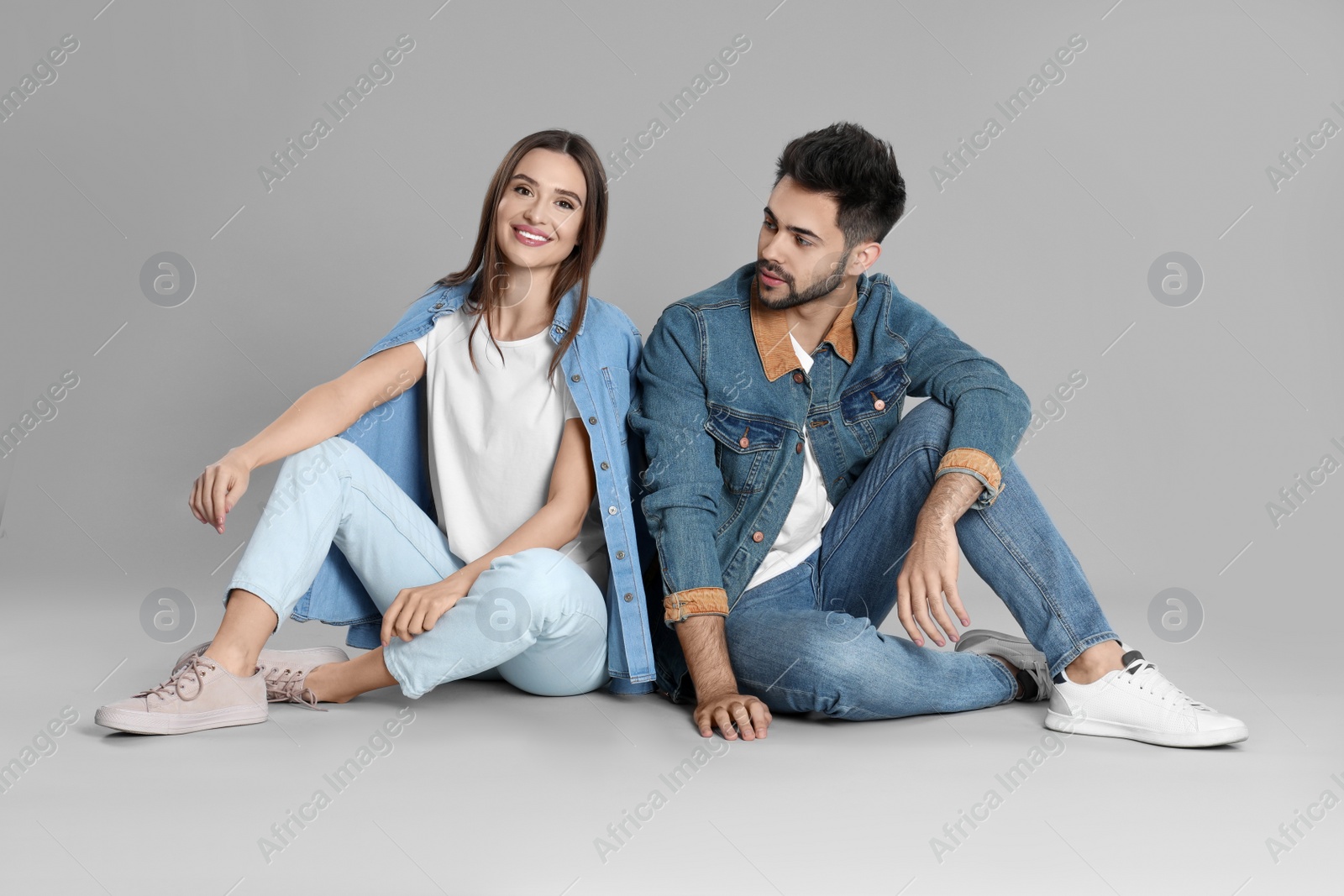 Photo of Young couple in stylish jeans sitting on grey background