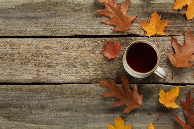 Photo of Cup of hot tea and autumn leaves on wooden table, flat lay. Space for text