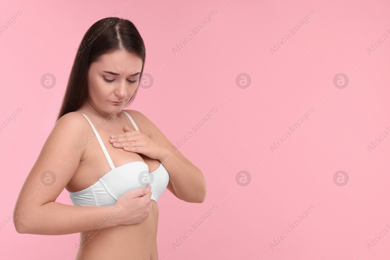 Photo of Mammology. Woman in bra doing breast self-examination on pink background, space for text
