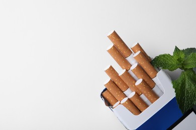 Photo of Pack of menthol cigarettes and mint on white background, top view. Space for text