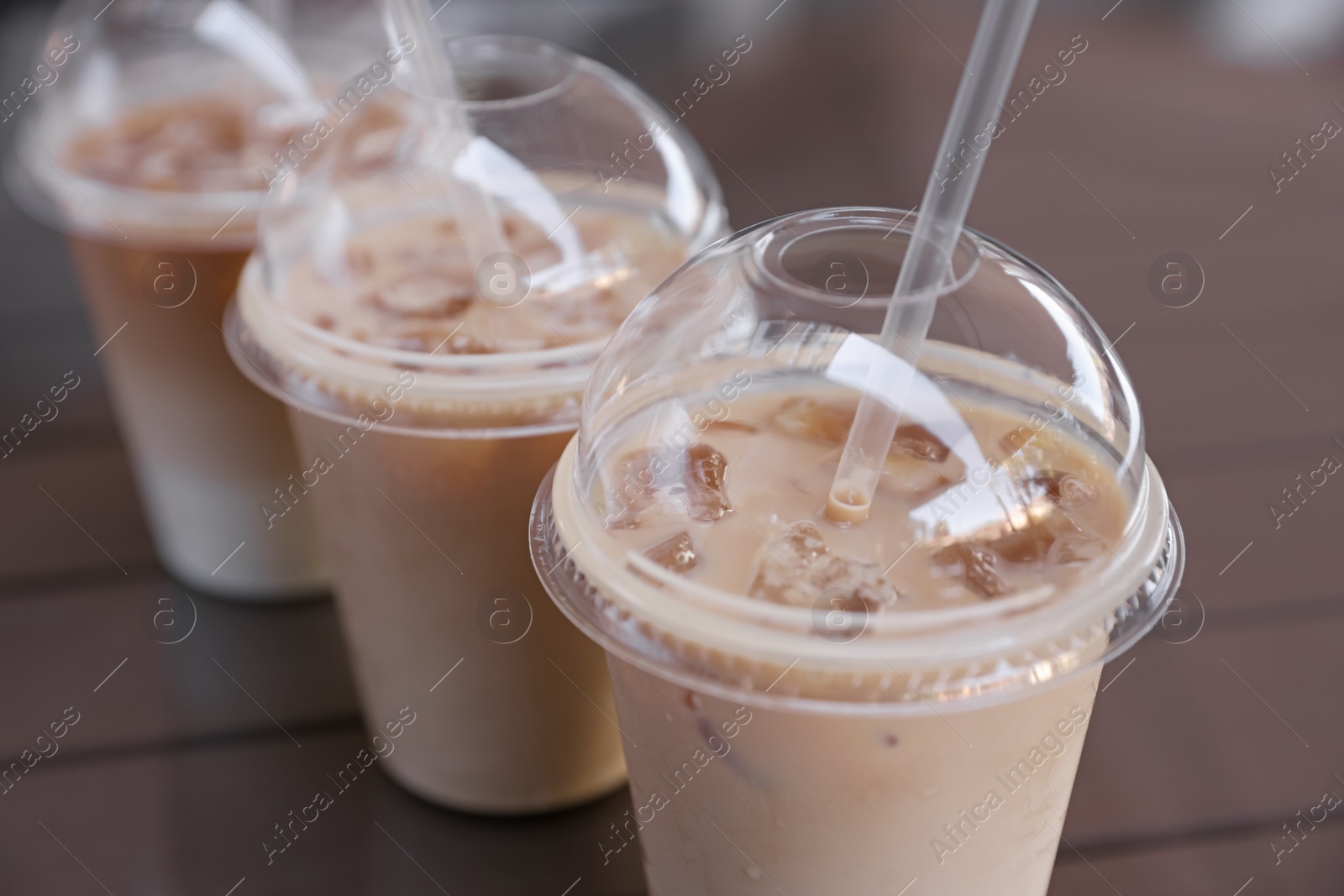 Photo of Plastic takeaway cups of delicious iced coffee on table, closeup