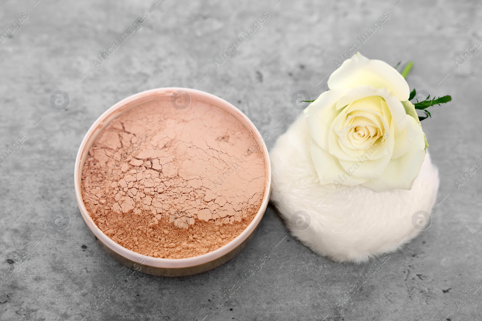 Photo of Face powder, puff applicator and rose flower on grey textured table, closeup