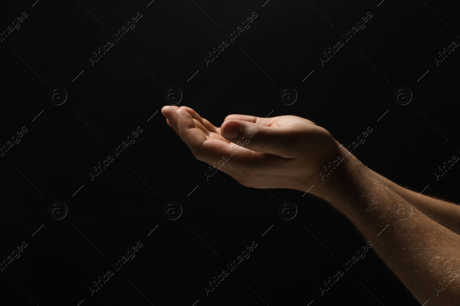 Photo of Religion. Man with open palms praying on black background, closeup. Space for text