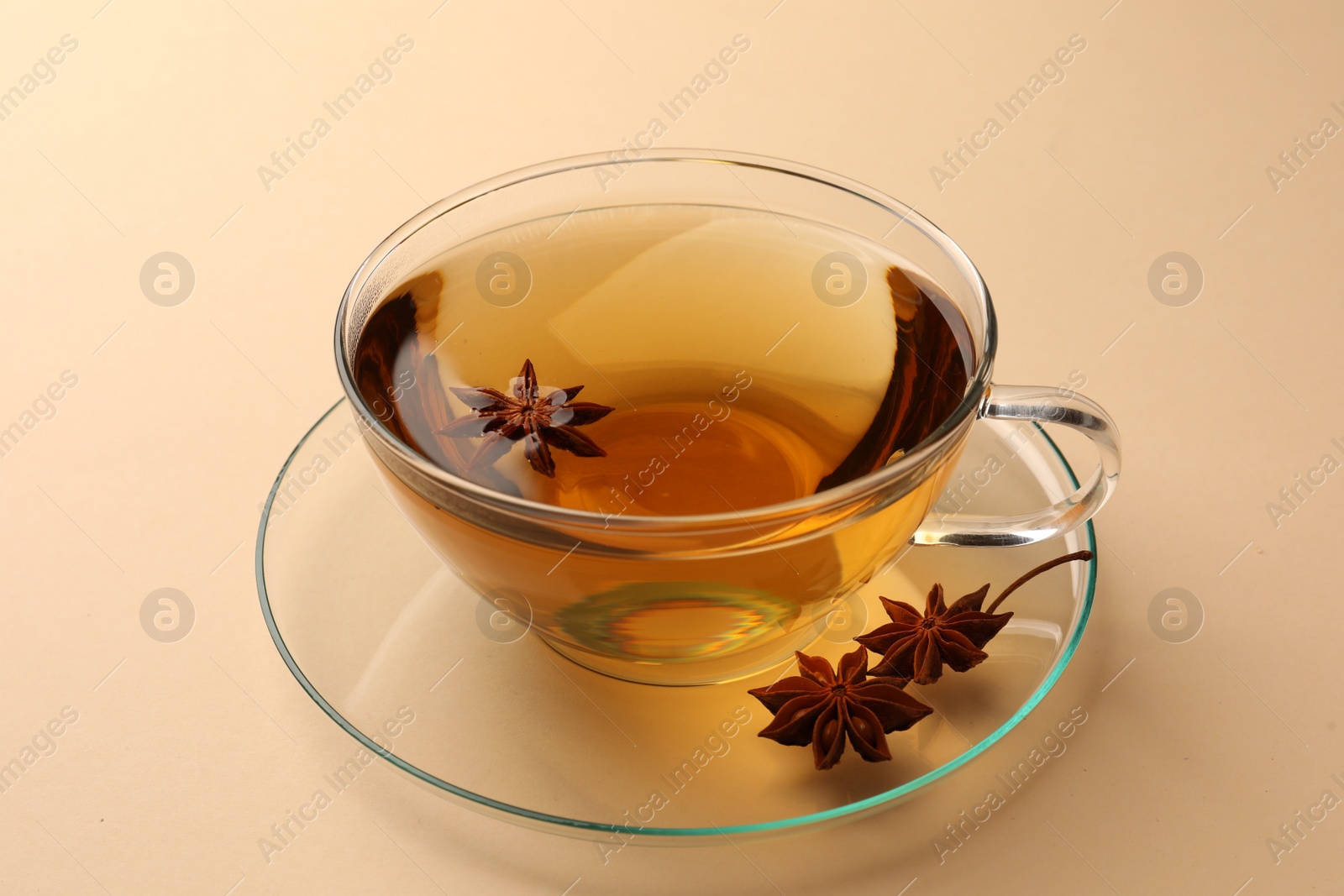 Photo of Glass cup of aromatic tea with anise stars on beige background