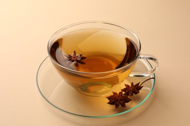 Glass cup of aromatic tea with anise stars on beige background