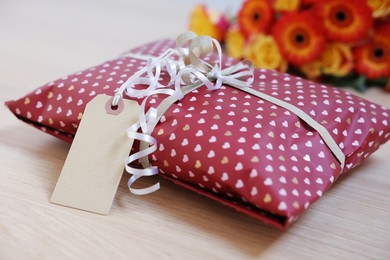 Photo of Parcel wrapped in heart patterned paper with cardboard tag on wooden table, closeup. Space for text