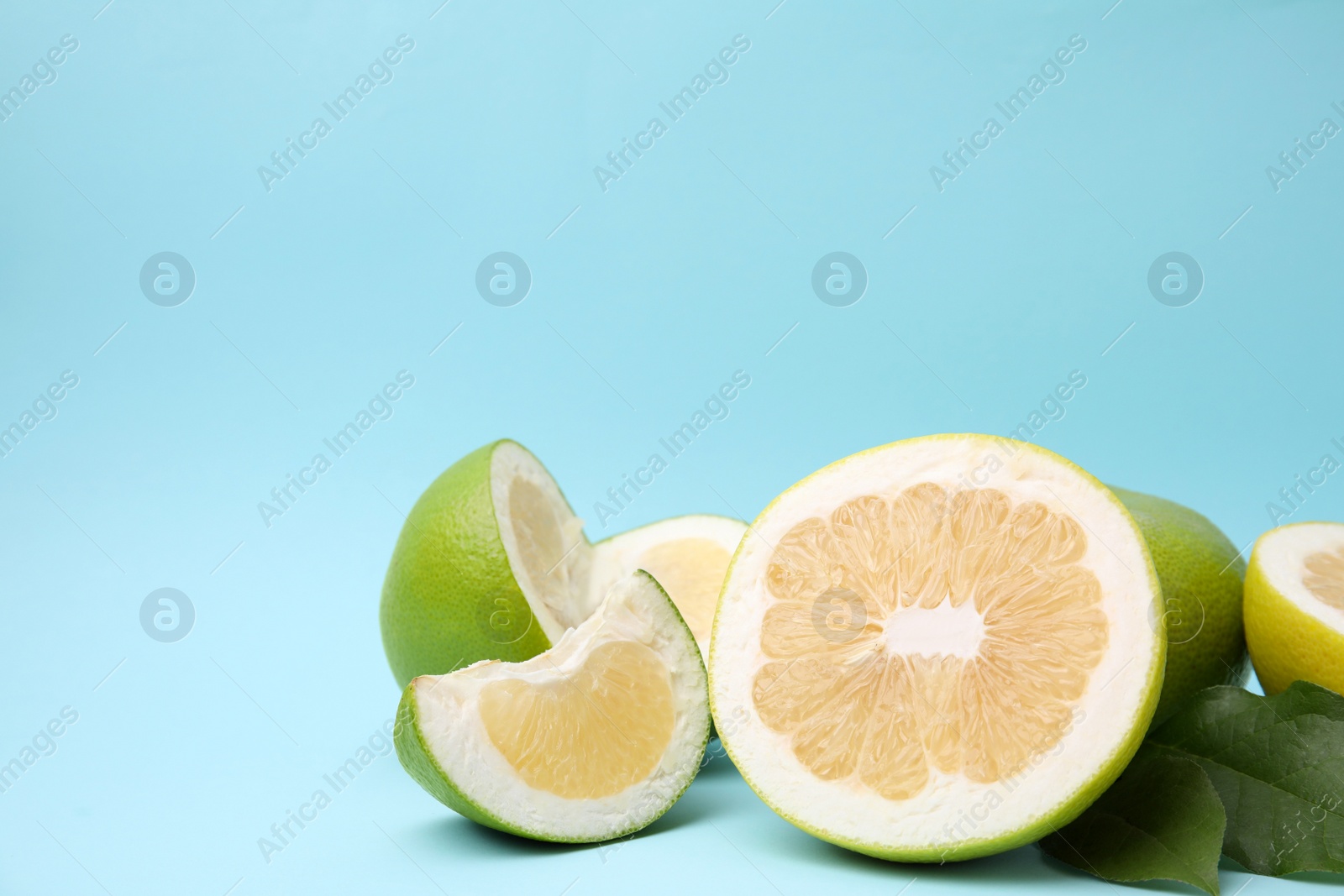 Photo of Whole and cut sweetie fruits with green leaves on light blue background. Space for text