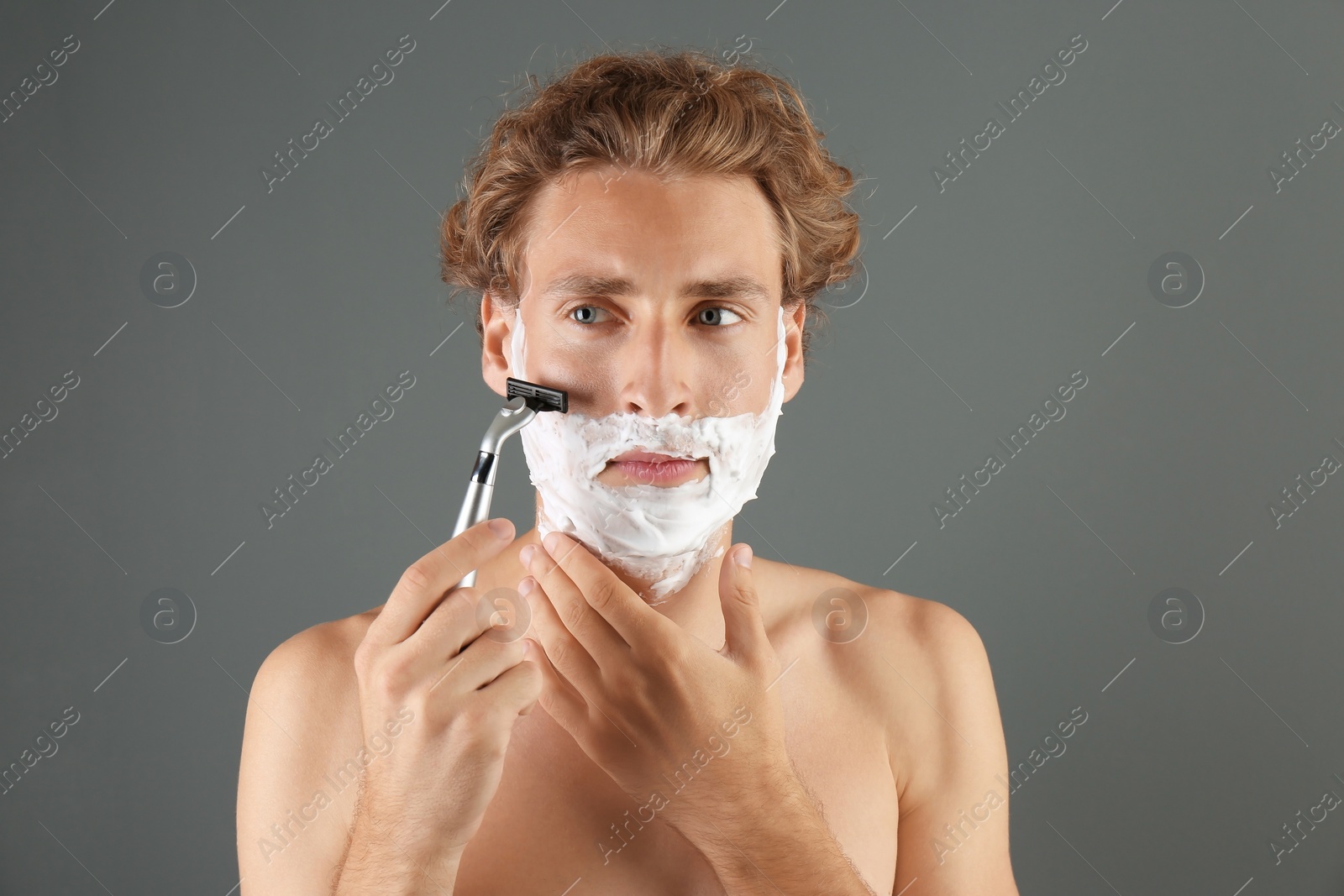 Photo of Handsome young man shaving on gray background