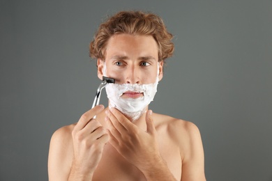 Photo of Handsome young man shaving on gray background