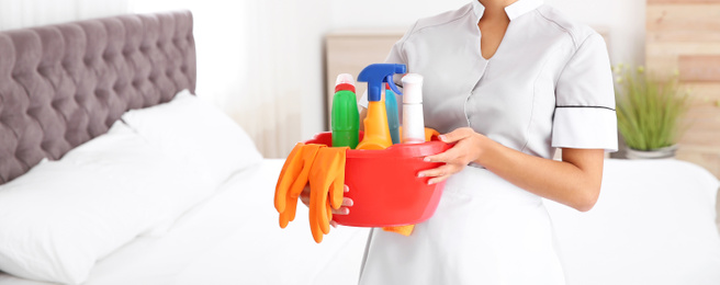 Image of Young chambermaid holding cleaning supplies in bedroom, closeup view with space for text. Banner design