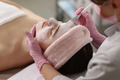 Photo of Cosmetologist applying mask on woman's face, closeup