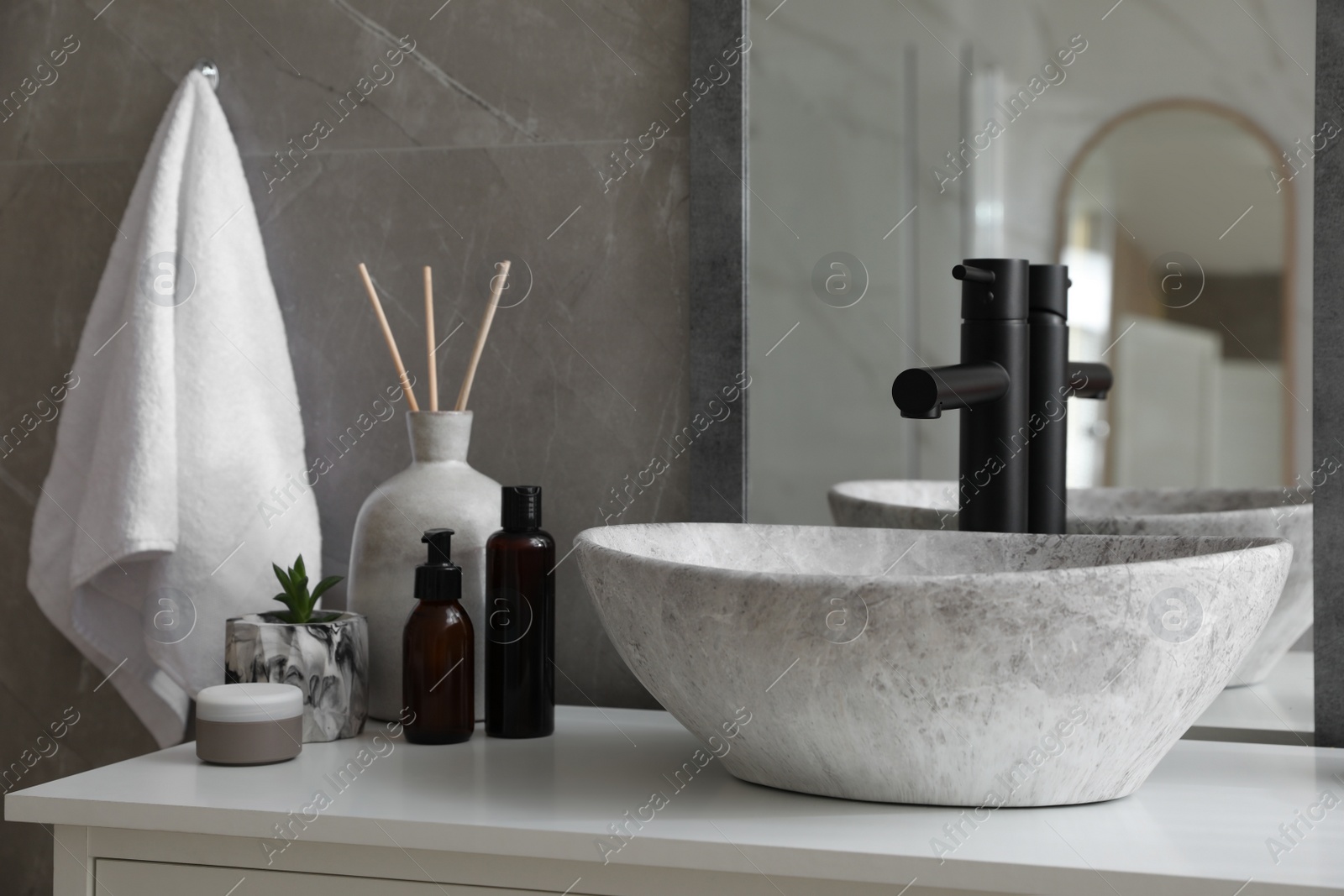 Photo of Stone vessel sink with faucet and toiletries on white countertop in bathroom