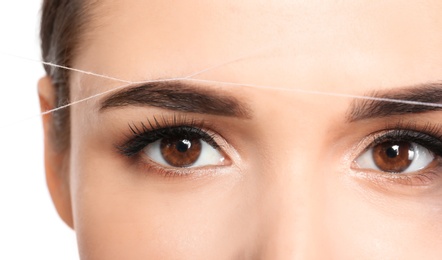 Young woman correcting eyebrow shape with thread, closeup