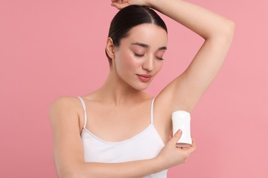 Beautiful woman applying deodorant on pink background