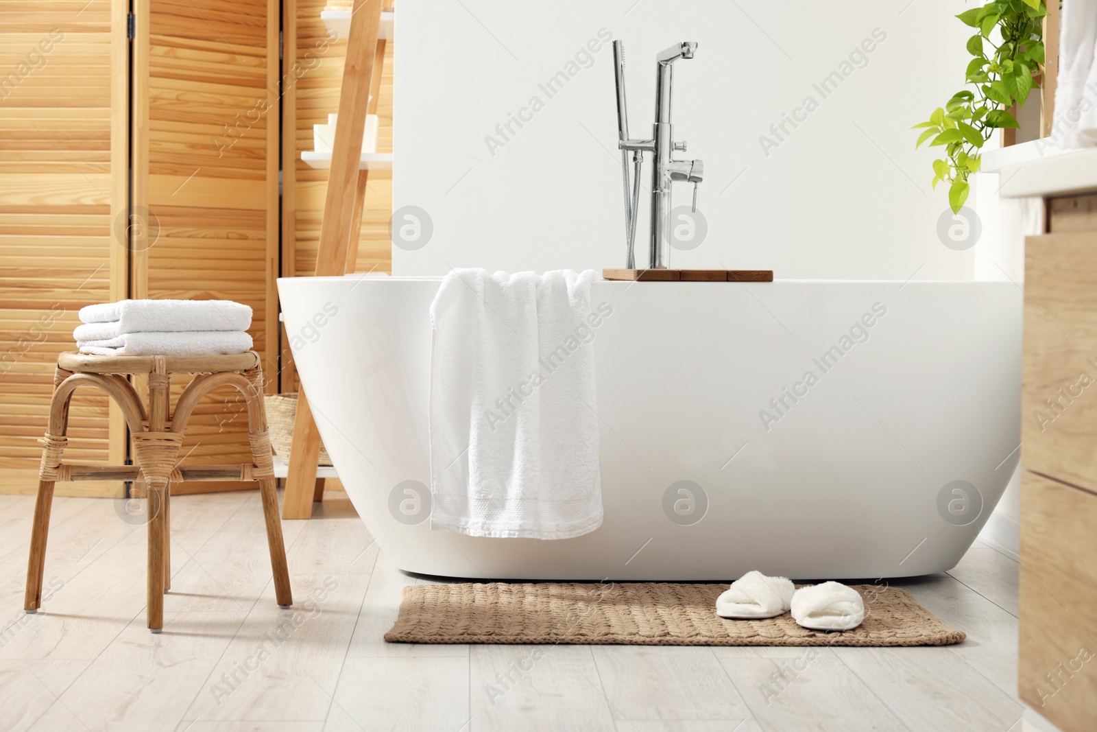 Photo of Stylish tub, wicker stool, slippers and soft towels in bathroom