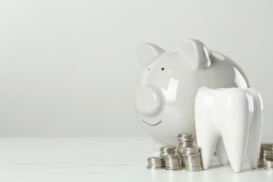 Photo of Ceramic model of tooth, piggy bank and coins on white table, space for text. Expensive treatment