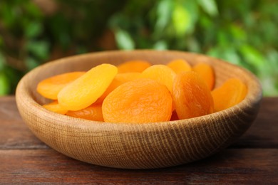 Bowl of tasty apricots on wooden table against blurred green background. Dried fruits