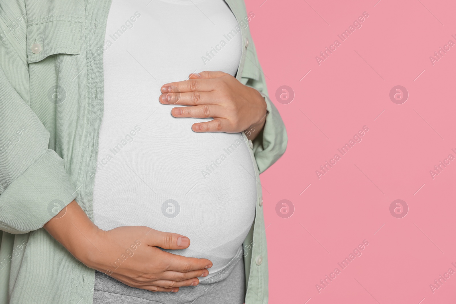 Photo of Pregnant woman on pink background, closeup. Space for text