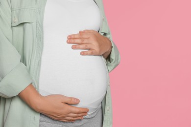 Photo of Pregnant woman on pink background, closeup. Space for text