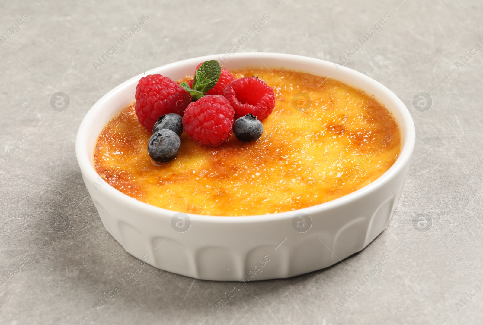 Photo of Delicious creme brulee with fresh berries on light grey table, closeup