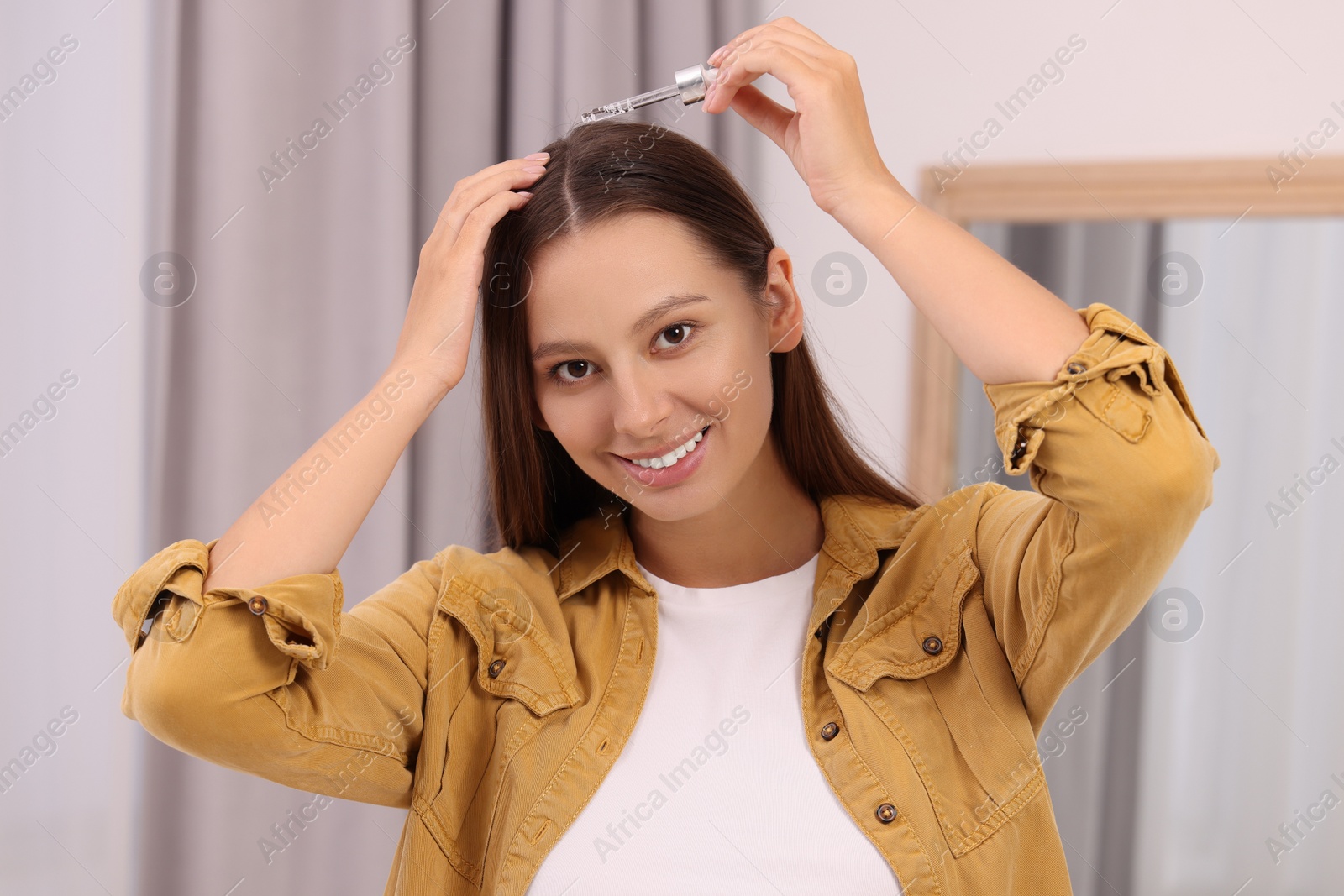 Photo of Beautiful woman applying serum onto hair indoors