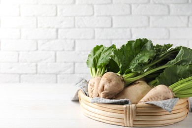 Photo of Basket with fresh sugar beets on white table near brick wall. Space for text