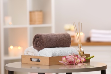 Photo of Tray with towels and reed air freshener on table in spa salon