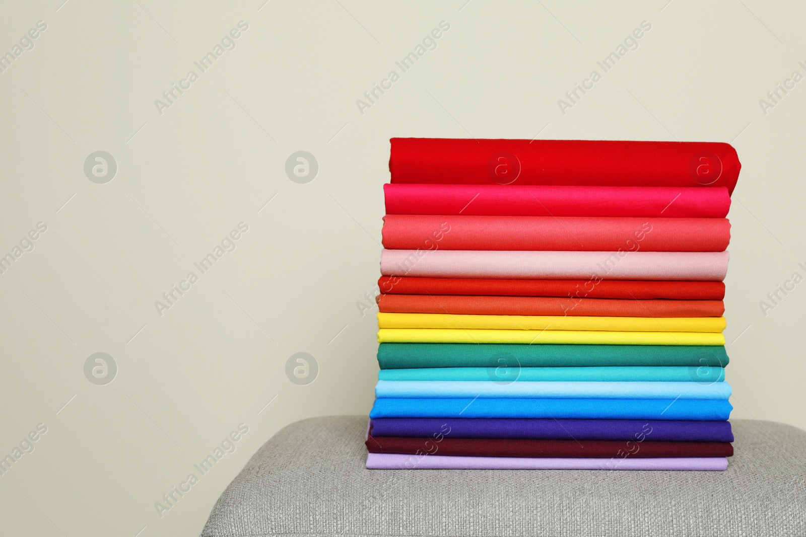 Photo of Pile of bright t-shirts on sofa against color background