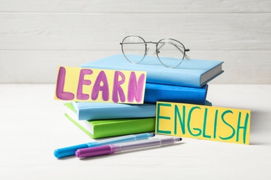 Photo of Phrase LEARN ENGLISH, books, glasses and felt tip pens on white wooden table