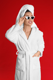 Photo of Beautiful young woman in bathrobe and sunglasses on red background
