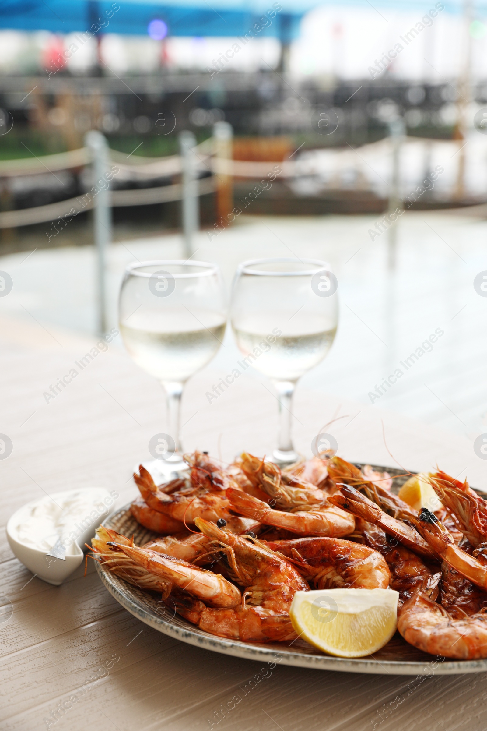 Photo of Plate of delicious cooked shrimps served with lemon and wine at table outdoors