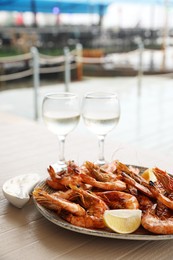 Photo of Plate of delicious cooked shrimps served with lemon and wine at table outdoors