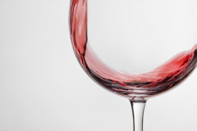 Pouring red wine into glass on light background, closeup