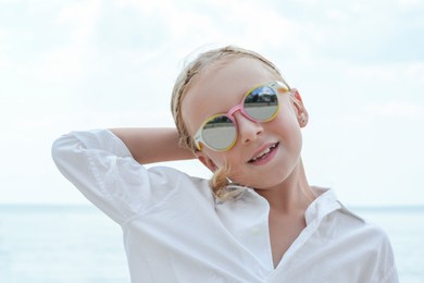 Photo of Little girl wearing sunglasses at beach on sunny day