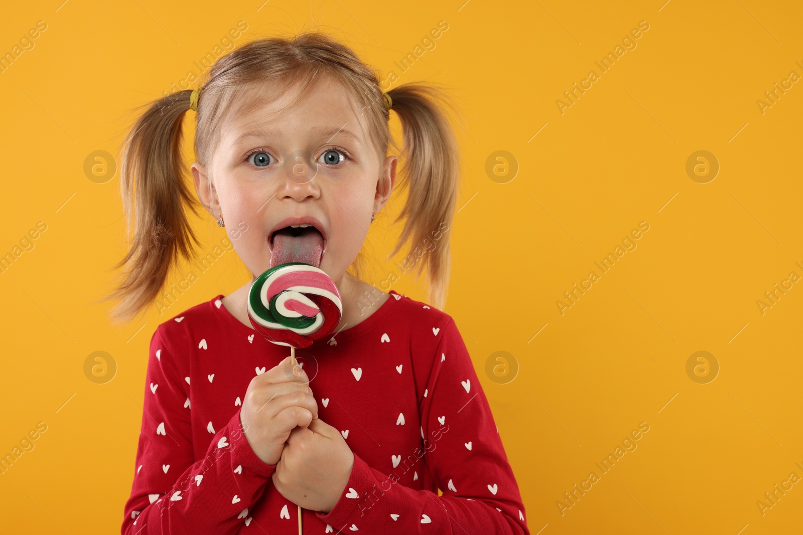 Photo of Portrait of cute girl licking lollipop on orange background, space for text