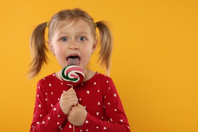 Photo of Portrait of cute girl licking lollipop on orange background, space for text