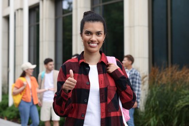 Photo of Happy student with backpack showing thumbs up outdoors, selective focus