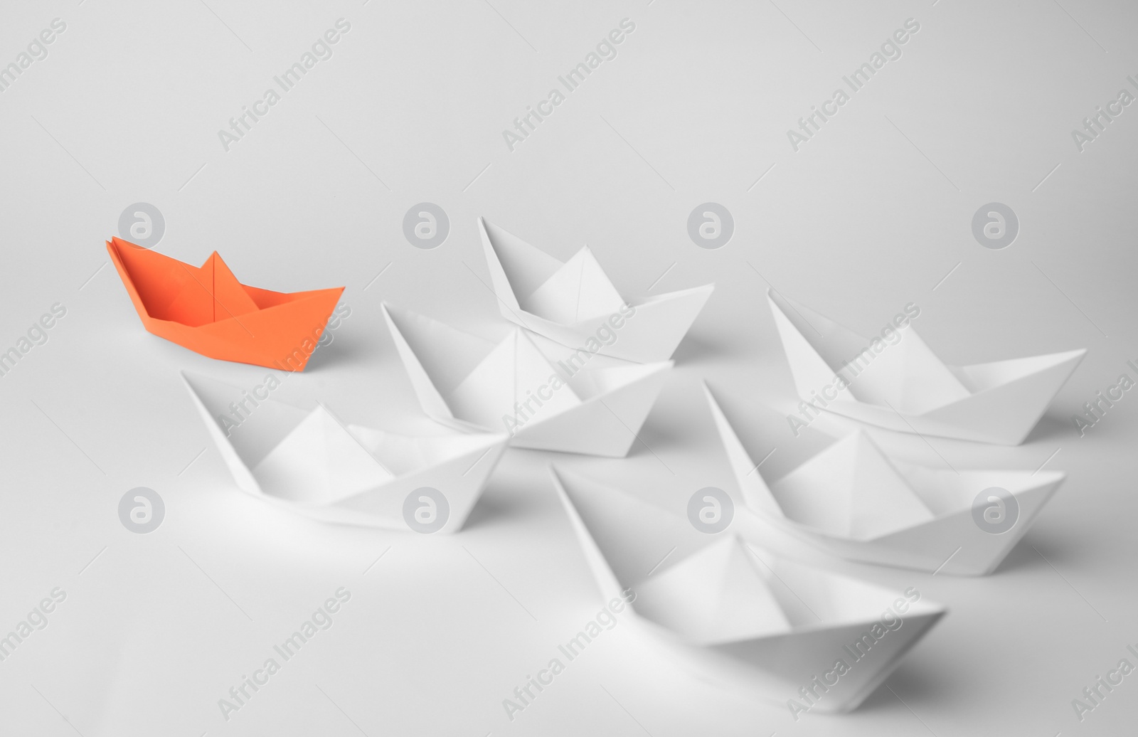 Photo of Group of paper boats following orange one on white background. Leadership concept