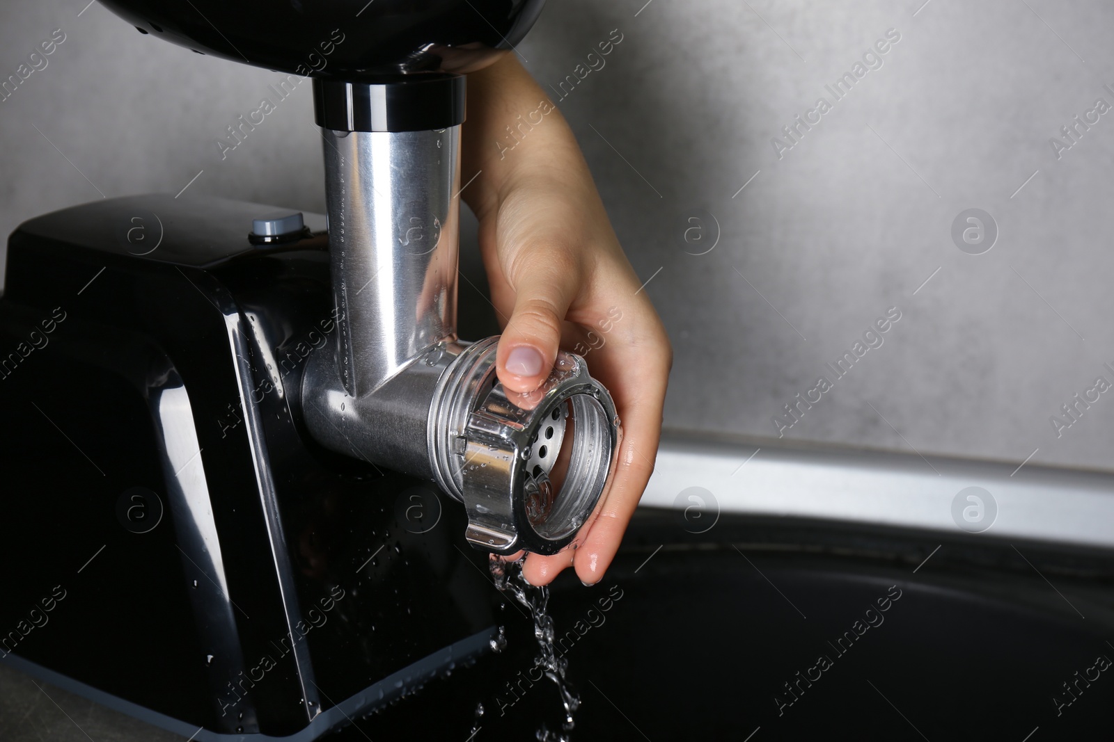 Photo of Woman washing electric meat grinder under kitchen sink, closeup. Space for text